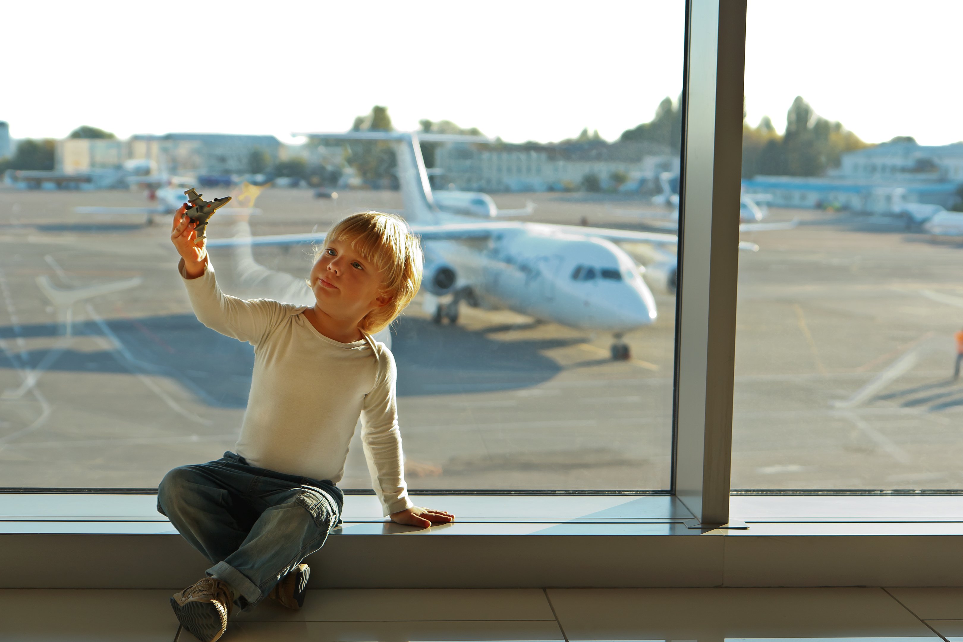 For family Reisen - Reiseziele 2024 - Junge mit Flugzeugspielzeug am Flughafen